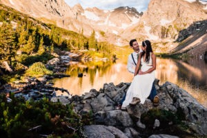 At this sunrise mountain elopement in Colorado, Tatum sits on her husband’s lap with her hiking boots peeking out below her dress, as they enjoy the alpen-glow on the mountains behind them.