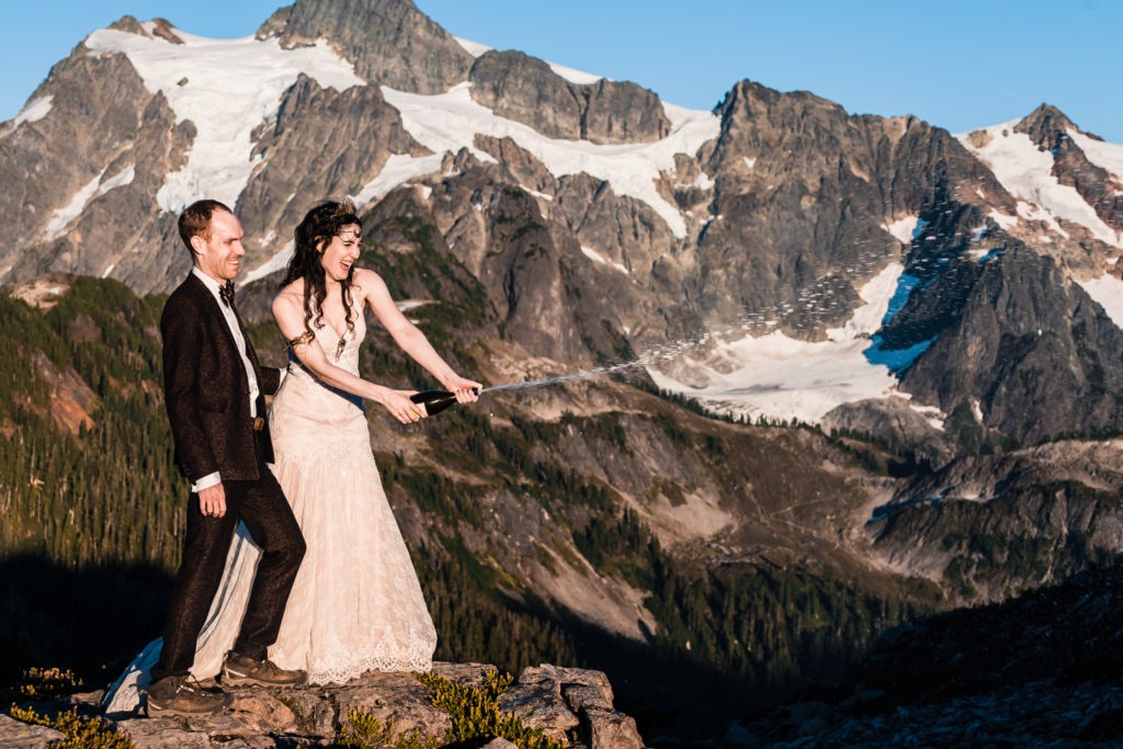 At this Washington elopement in the North Cascades, the couple pop champagne to celebrate, with dramatic snow-capped mountains rising in the background.