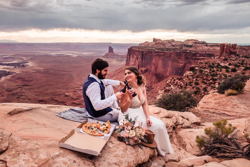 Moab wedding with pizza and beers. The couple enjoy their favorite food and drink as they watch the sunset at Canyonlands.