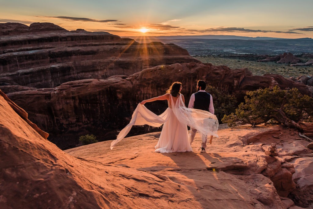 Sunrise wedding in Moab, Utah. The sun rises over a long ridge or red rock, creating a golden glow across the whole landscape.