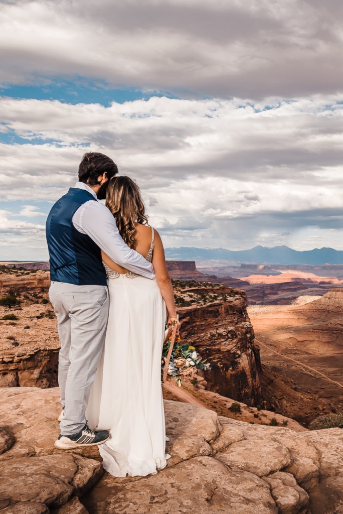 Moab wedding. The couple cuddle as they take in the insane views.