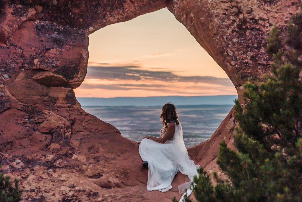 Sunrise wedding with a badass bride! Crystal sits inside a window in the rock to watch the sun rise over Arches National Park, Moab.