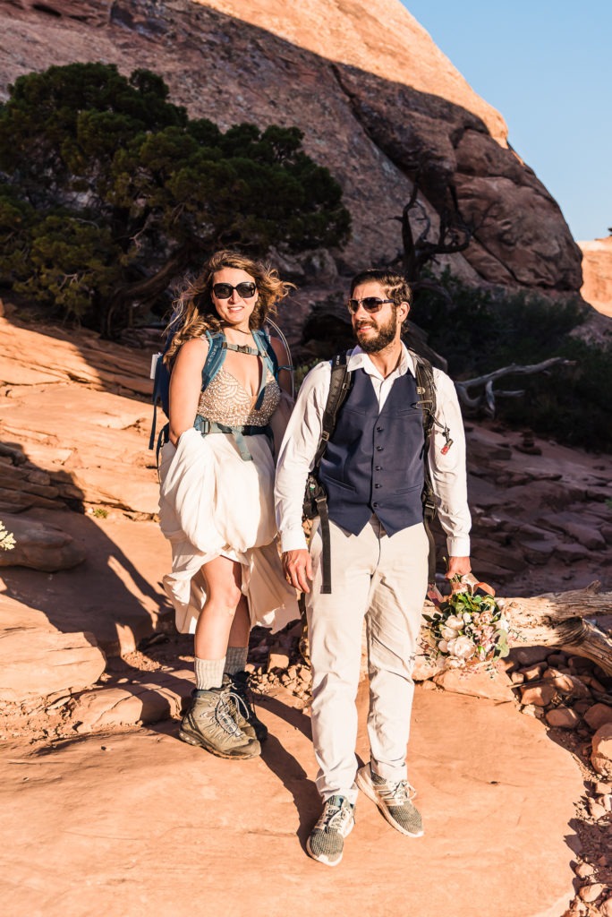 Hiking wedding in Utah. This super cool couple with sunglasses and backpacks get ready to explore Arches National Park.