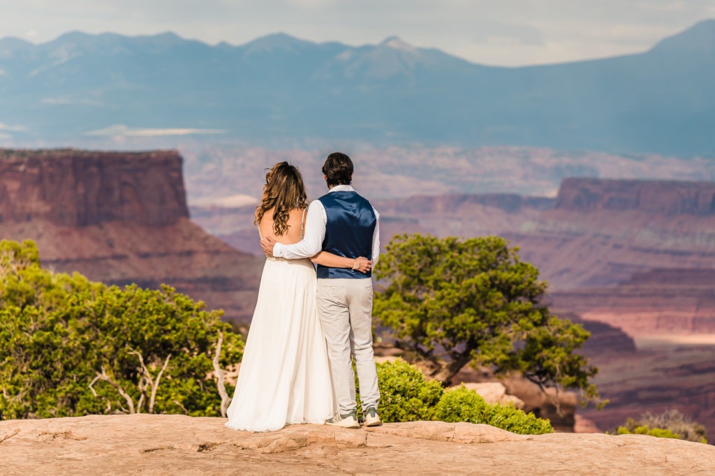 Moab wedding. The couple stand side by side with their arms around each other as they take in the incredible views.