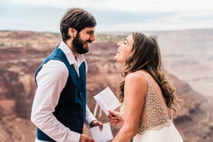 Moab wedding, Utah. A young couple share their wedding vows at their Moab elopement. He is smiling as she lets out a huge laugh!