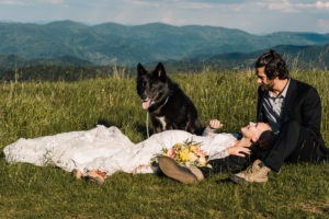 At this North Carolina wedding with their dog, the bride and groom lie down in the lush, green grass together, with their beautiful black wolf-dog cuddled up with them. Layers upon layers of green mountains fill up the horizon.