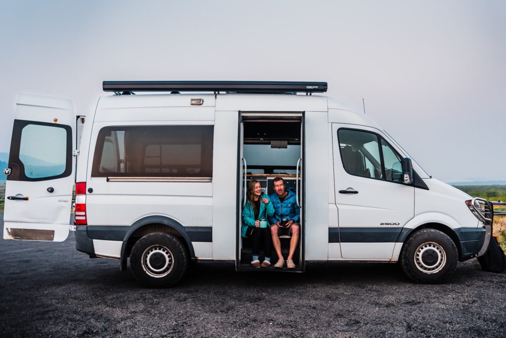 A couple sit in the door of their renovated van as they wait for the sun to rise and their wedding adventure to begin.