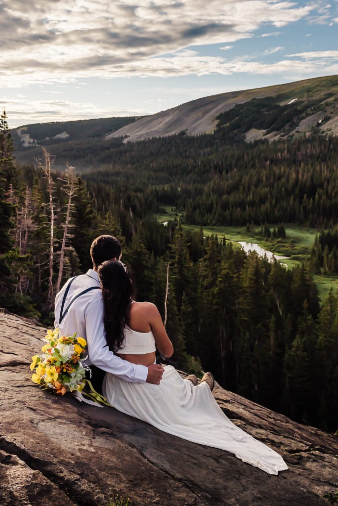 Sunrise wedding. The couple sit on the edge or a rock in the mountains and enjoy the views just after sunrise.
