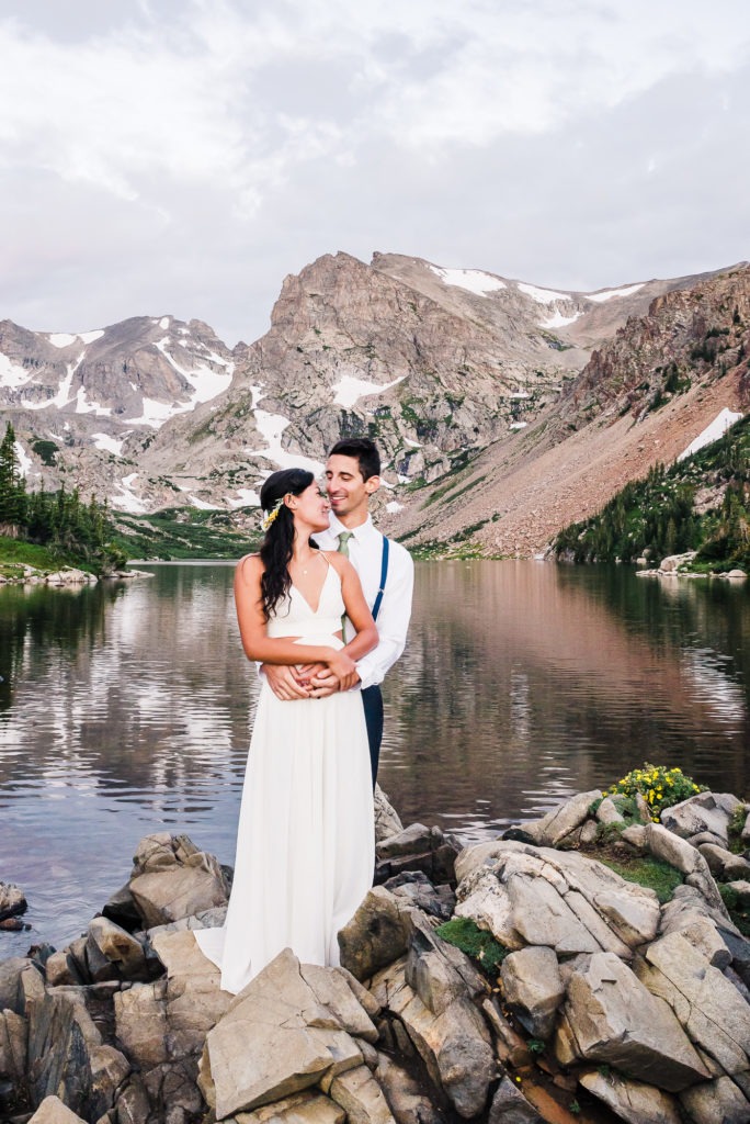 Colorado mountain wedding. The couple cuddle together by the side of a lake, with the mountains reflecting in the water.