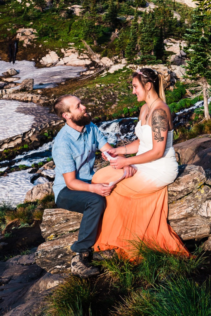 The bride to be wears a white dress with a dip-dyed orange bottom half and sits with her fiance as they share love letters during their mountain engagement shoot.