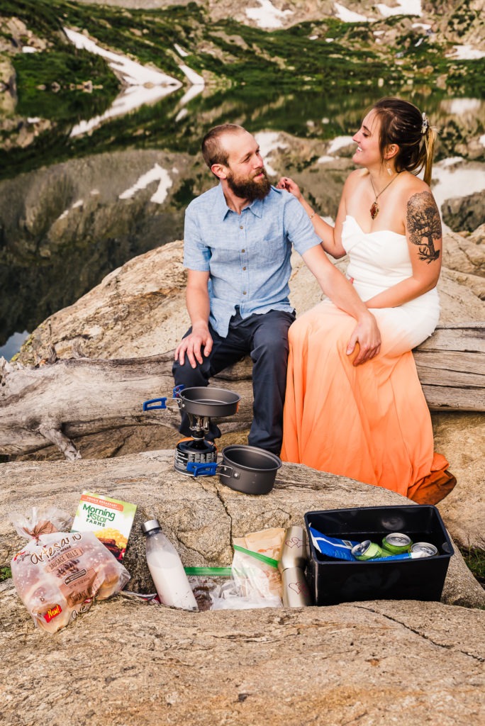Colorado adventure engagement. The couple sit together on an old log and cook breakfast over a camp stove.