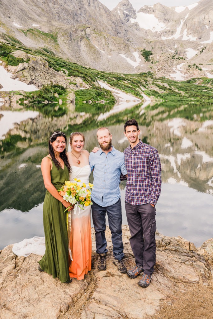 Colorado mountain engagement. 4 best friends celebrate their adventure at a stunning Colorado alpine lake, with the mountains reflected in the crystal clear water.