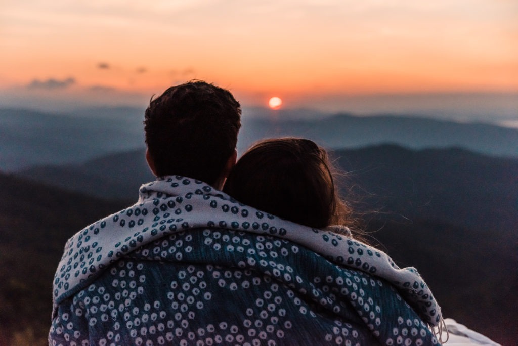 Sunrise wedding. The couple snuggle up with a blanket wrapped around to watch the sunrise over the mountains as they prepare to share their vows.