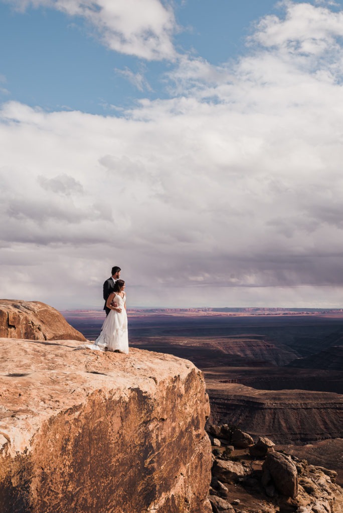 Utah wedding in Moab. The couple stand together on the edge of a canyon.