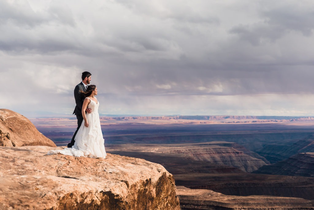 Moab elopement with insane views. The couple cuddle together and look out over the canyons.