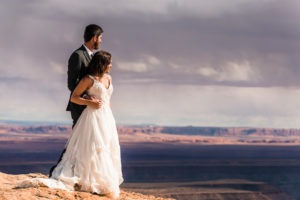 Moab wedding. The couple look out over canyons as a storm rolls in in the distance, creating a moody dramatic sky.