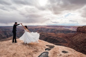 Moab wedding, utah. The couple share a first dance overlooking dramatic canyons. Her multi-layered dress swooshes as he spins her.