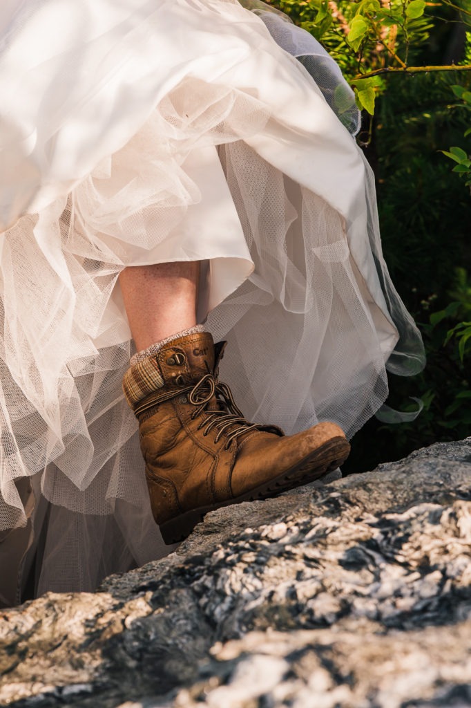 Close up of the bride's hiking boots as she lifts her dress up to climb a rock.