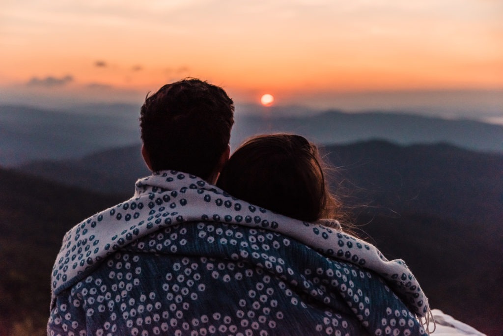 The couple cuddle in a cute blanket and watch the sun peep over the horizon.