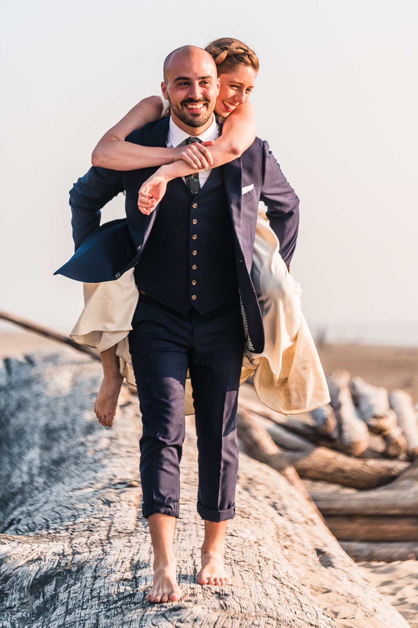 Olympic National Park wedding. As they play on the beach to celebrate their elopement, the groom gives his new wife a piggy back along a giant washed up log.