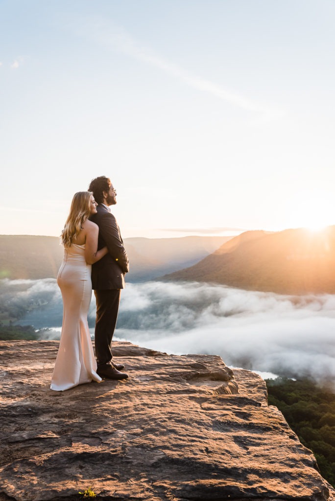 Sunrise Tennessee elopement. The bride in a sleek, form-fitting dress snuggles into the back of her groom as they look out at the sunrise together.