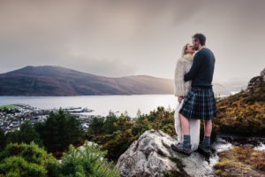 Scotland elopement. The couple snuggle up and share a kiss overlooking the small fishing village of Ullapool.