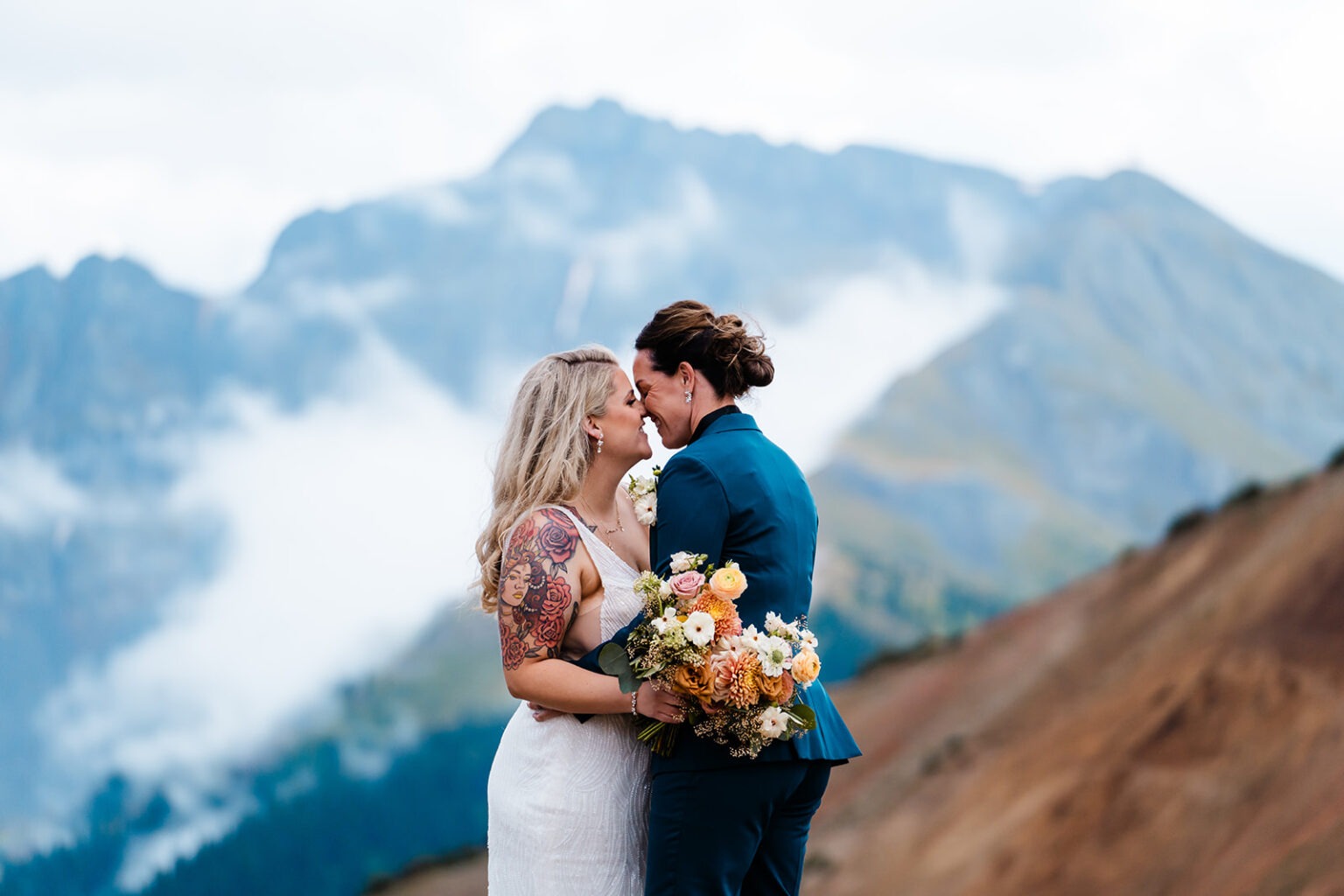 A wedding couple standing nose to nose about to kiss in the mountains