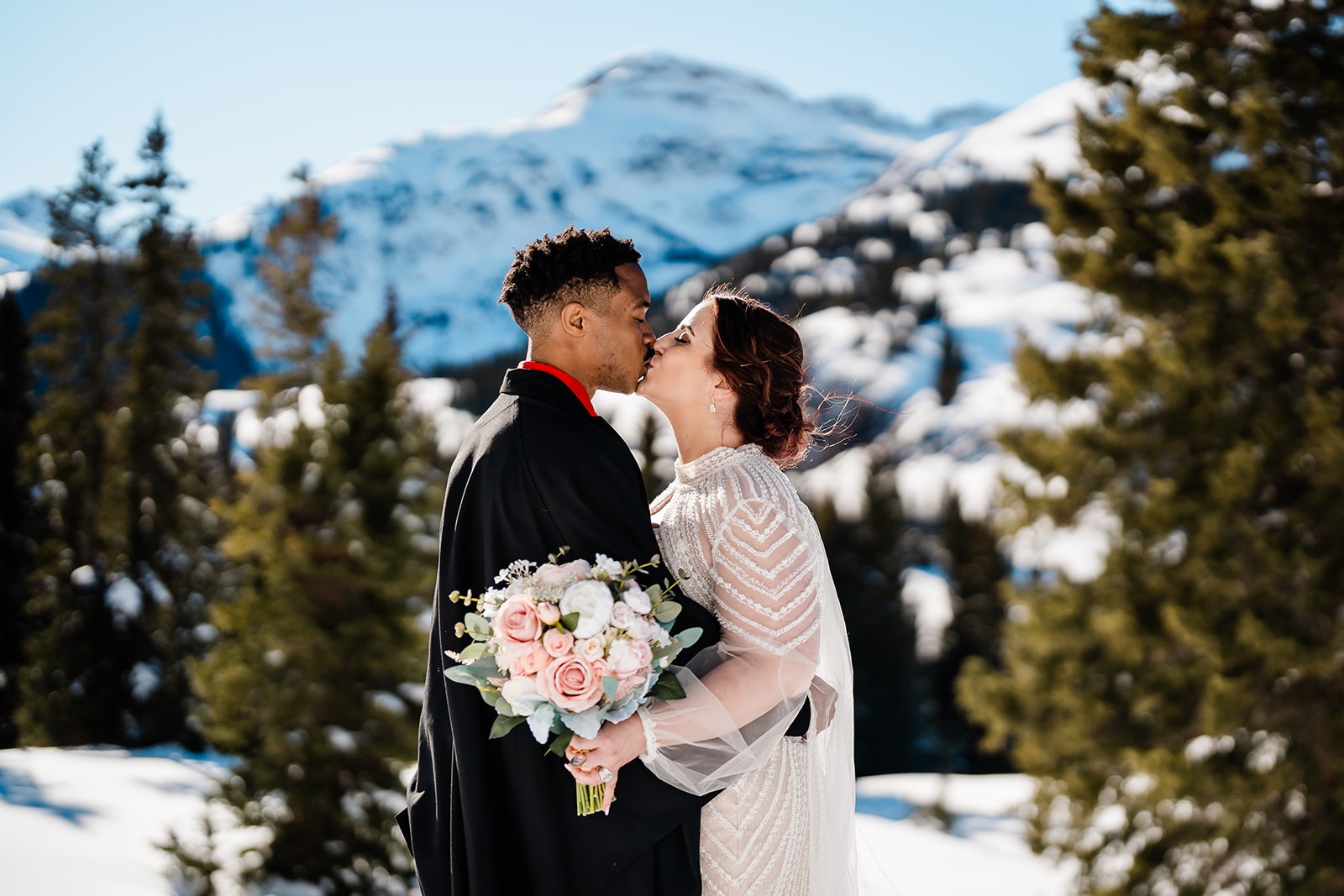 A wedding couple kissing in the mountains as one holds a bouquet of flowers