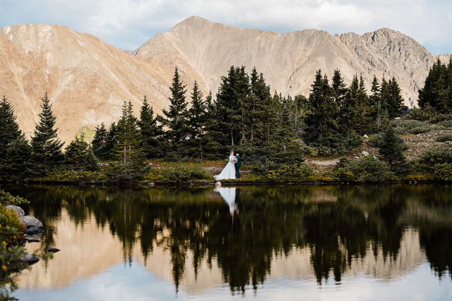 The view from across a lake of a newlywed couple standing close together