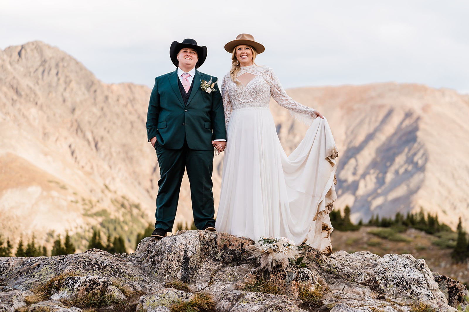 A newlywed couple standing on a rock in cowboy hats smiling together