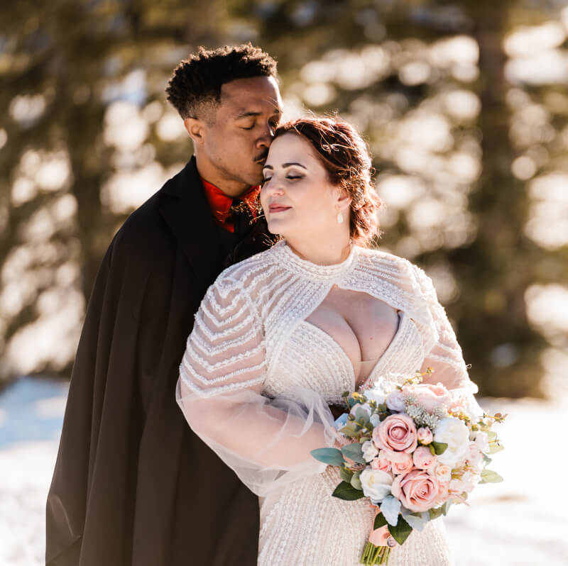 A couple leans into one another surrounded by snow.