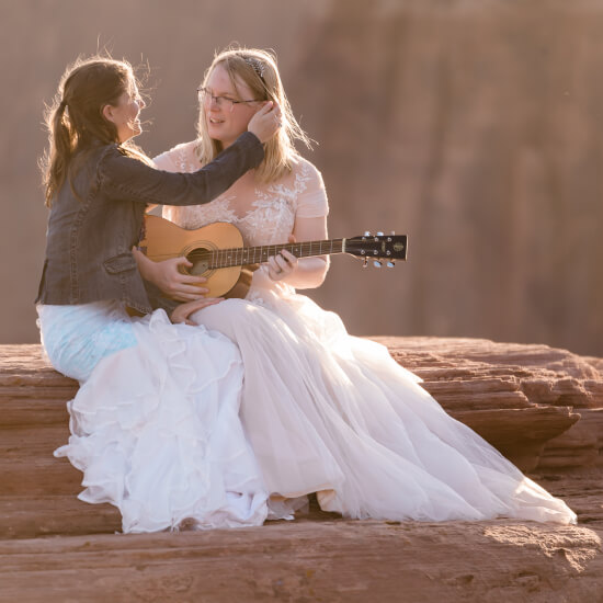 A couple sits on a fallen tree while one of them plays music.