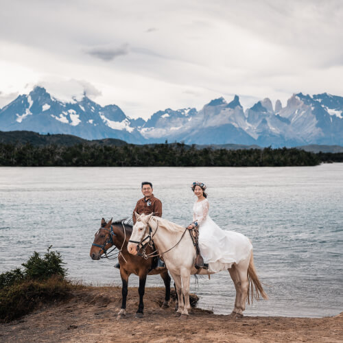 A couple rides horses surrounded by a lake and mountains on their elopement day.