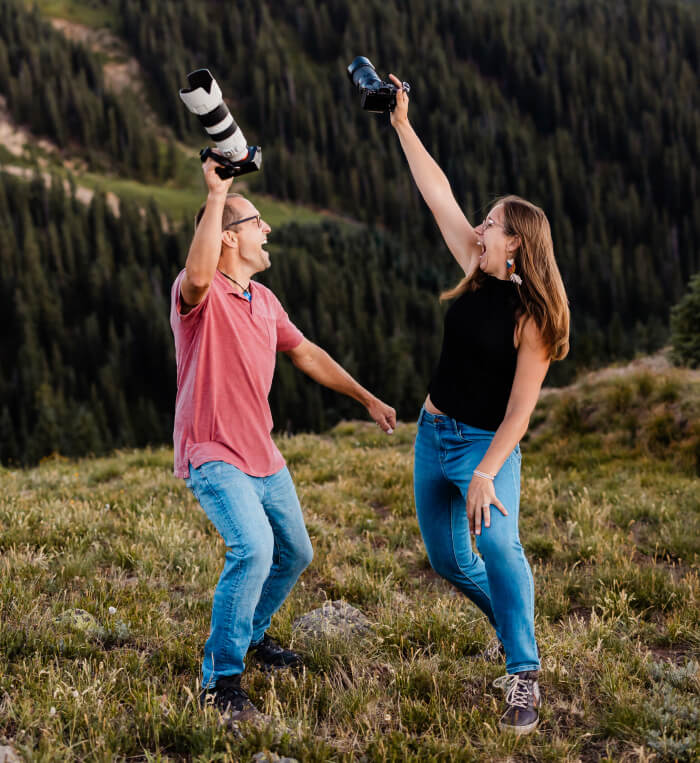 Chad and Vanessa smile while holding their cameras in the air, surrounded by Colorado landscapes.