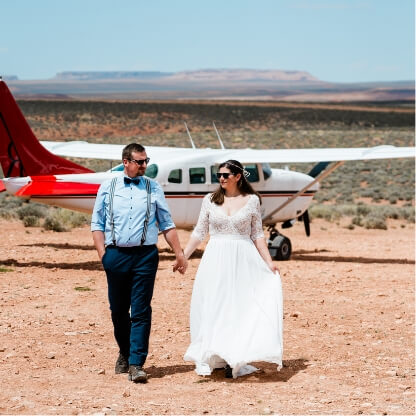 Two people hold hands walking away from a small red and white plane.