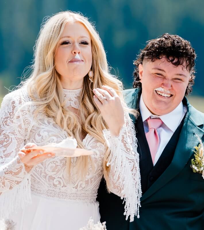 A couple smiles with cake on their noses.