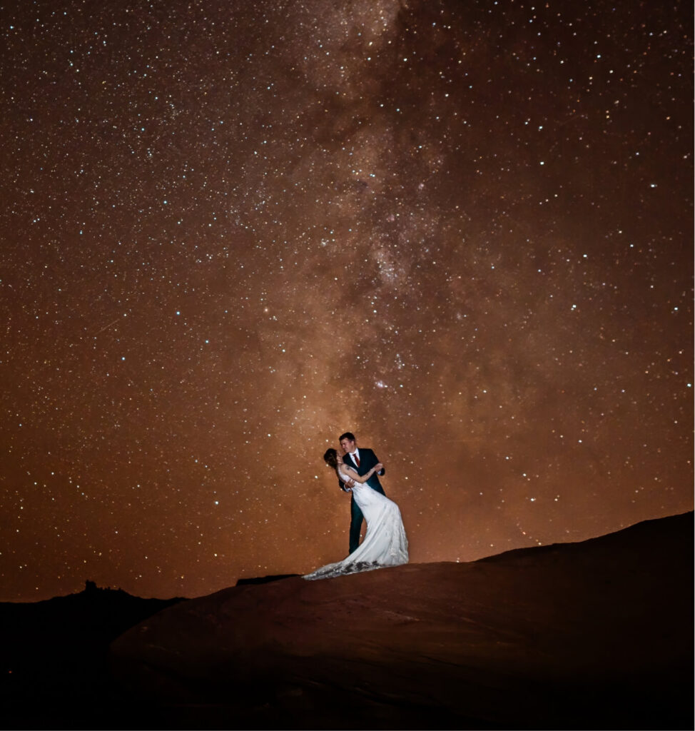 A person dipping their partner on their wedding day with a starry night sky behind them