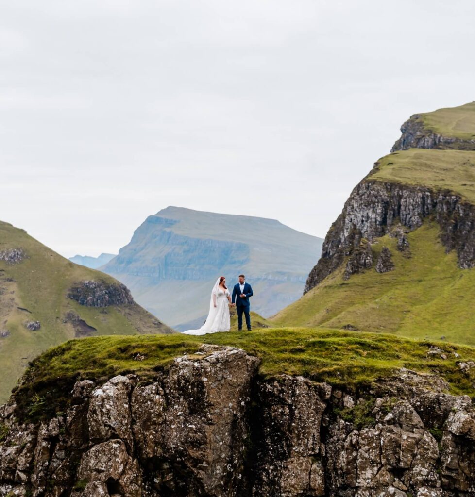 A couple standing on a grassy cliff holding hands on their wedding day