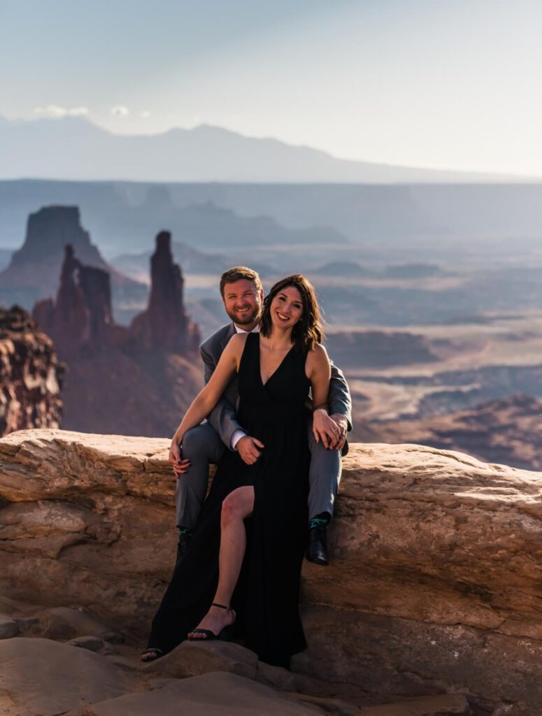 A couple sitting close together on the edge of a canyon overlook