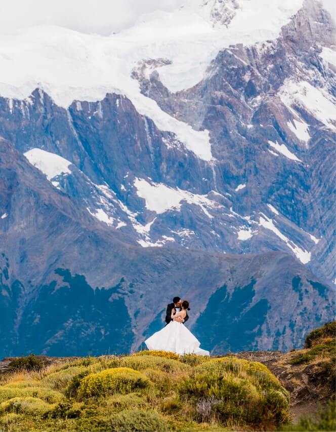 Two marriers kiss one another with snow-topped mountains just beyond.