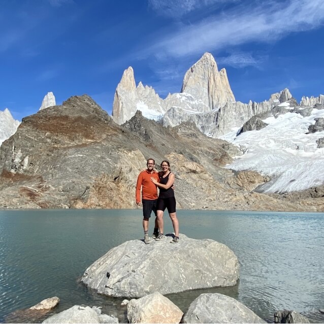 Chad and Vanessa stand on a rock surrounded by a blue lake.