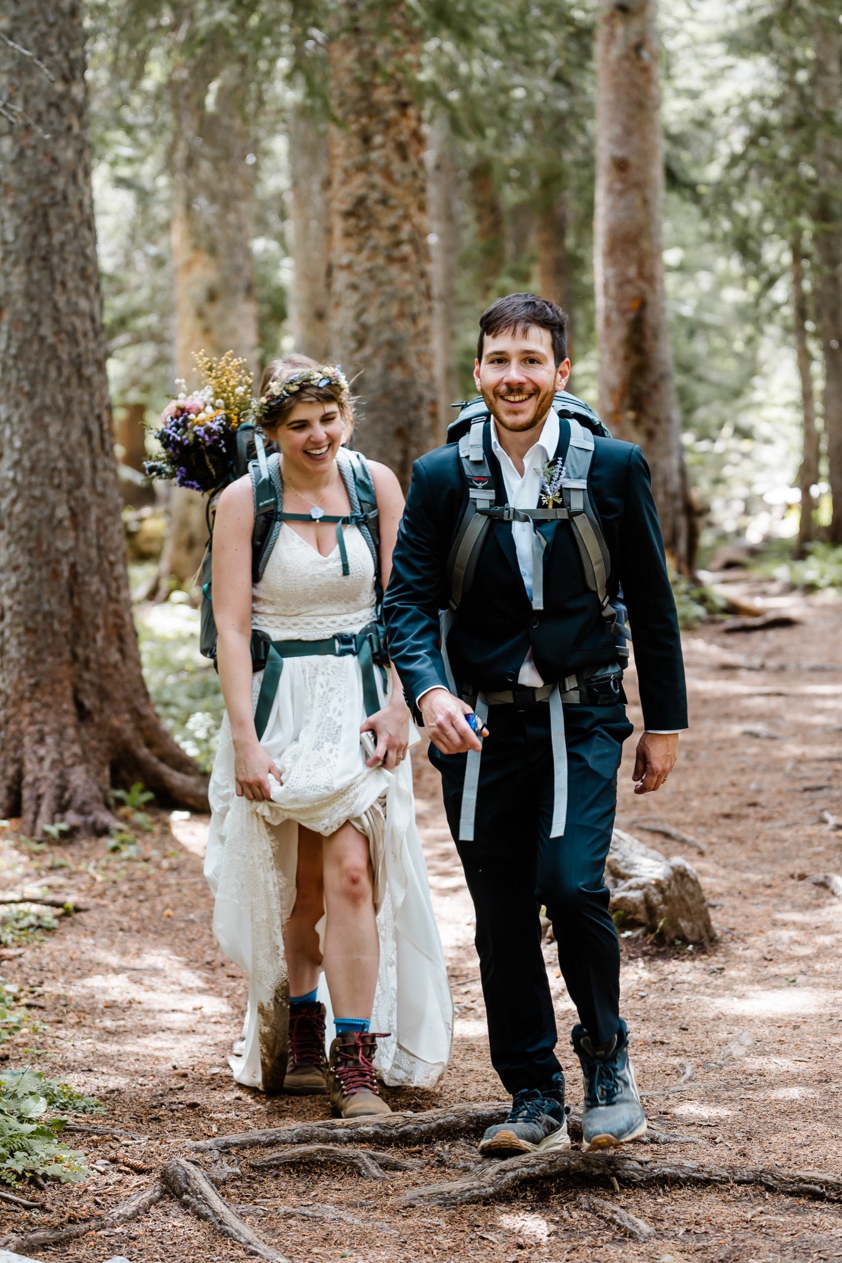 A newlywed couple hiking in the mountains with backpacks on while smiling