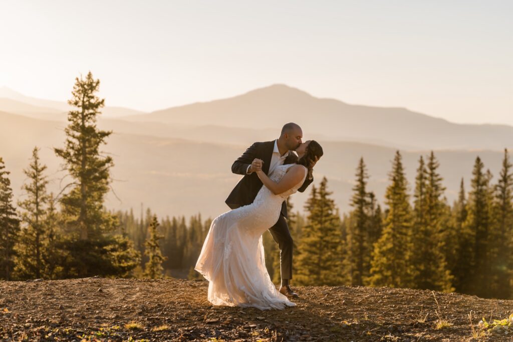 A person dipping their new spouse and kissing them on a mountain overlook