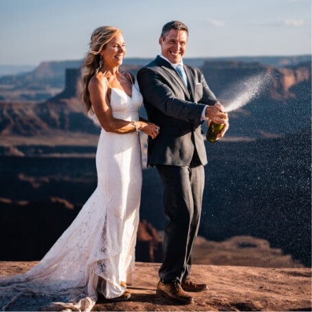 A couple does a champagne pop in the desert.