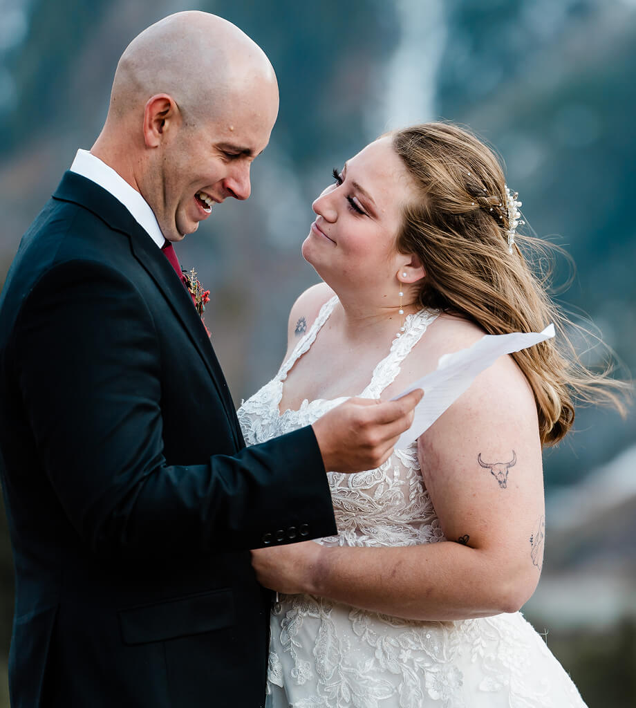 A person in a suit smiles while looking at vows, their partner looking at them.