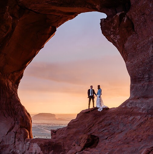 A couple standing in the middle of a rocky arch holding hands on their wedding day